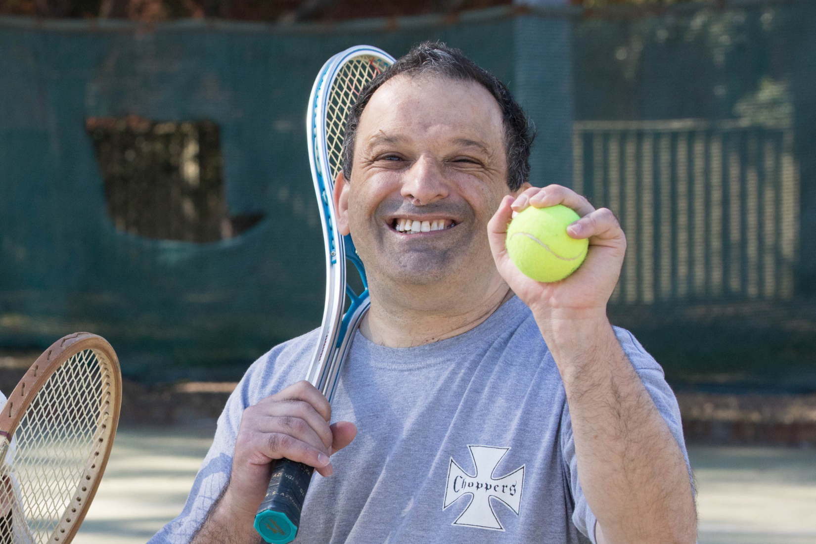 A man is playing tennis, he holds a racquet over his shoulder and is holding up a tennis ball in one hand. 